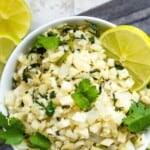 A bowl of cilantro lime cauliflower rice garnished with fresh cilantro and lime wedges.