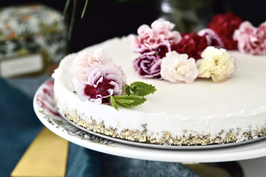 A vegan mint ice cream cake topped with fresh flowers on a cake stand.