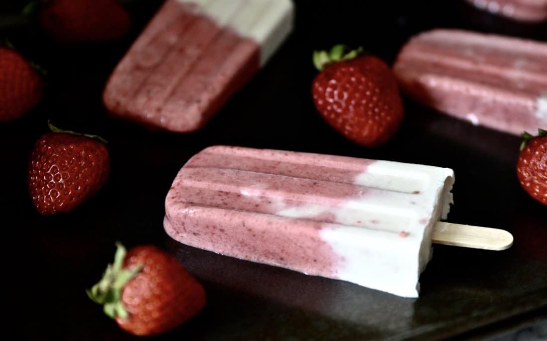 A strawberry vanilla popsicle surrounded by strawberries. 
