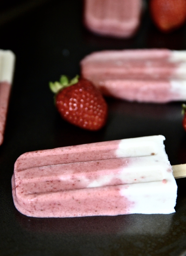 A strawberry vanilla popsicle in a row with other popsicles.