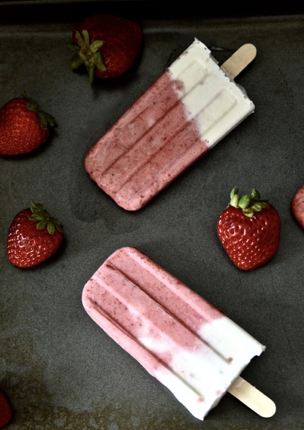 Two strawberry vanilla popsicles surrounded by strawberries.