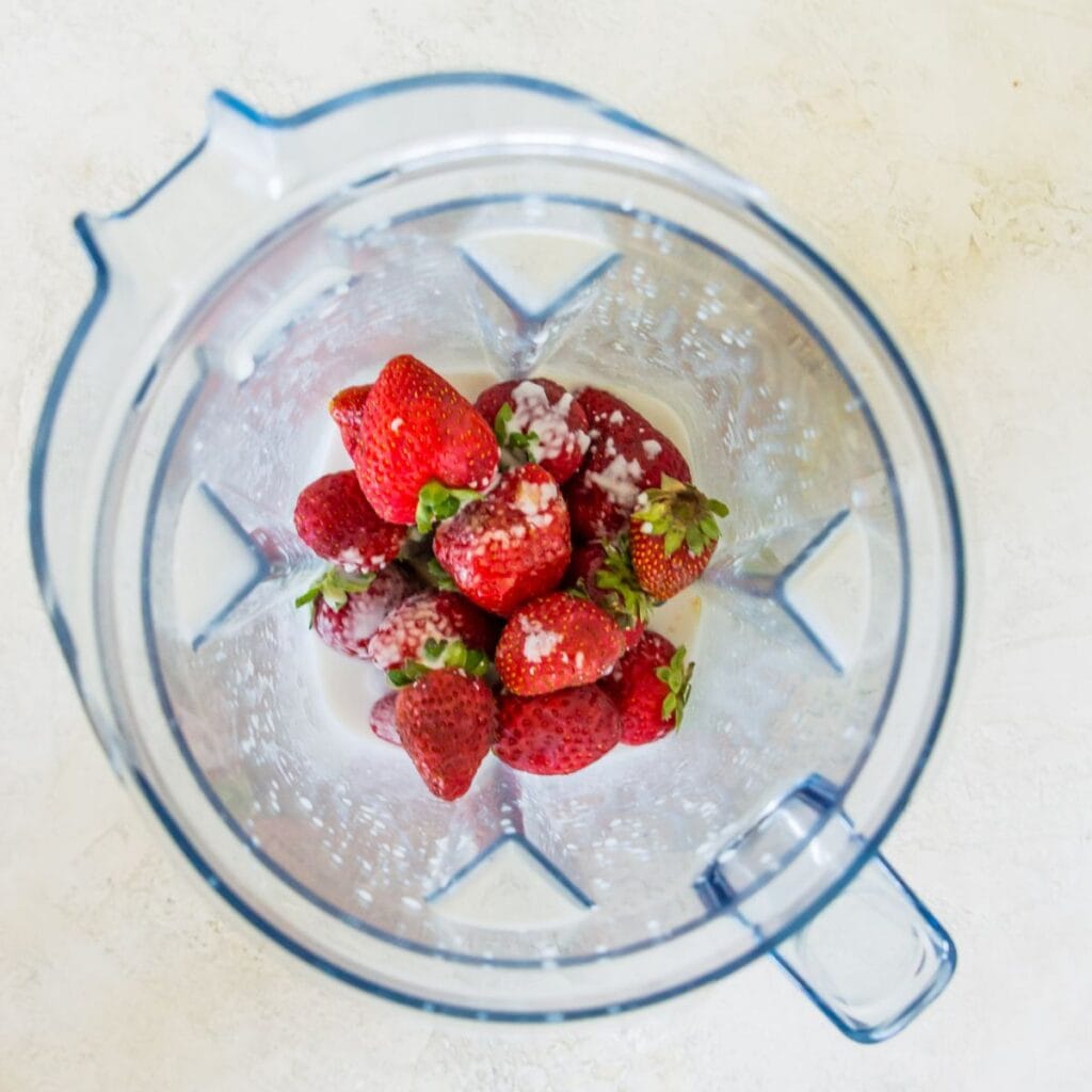 A blender filled with strawberries and milk.