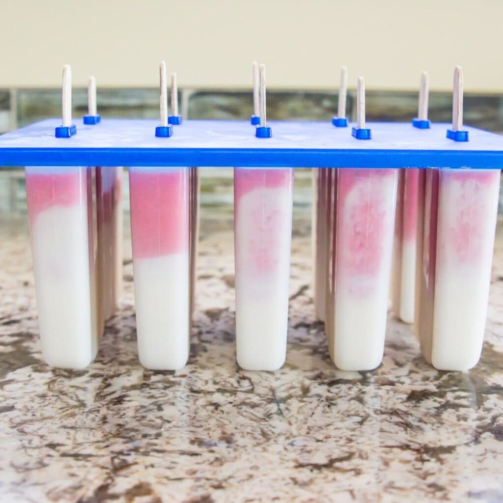 A popsicle mold filled half and half with a white and pink liquid.