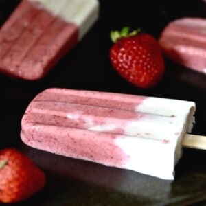 A pan with strawberry vanilla popsicles on it, with fresh strawberries around them.