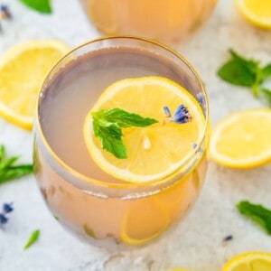 A glass of lavender mint lemonade topped with a lemon slice, mint leaves and lavender flowers.