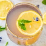 A glass of lavender mint lemonade topped with a lemon slice, mint leaves and lavender flowers.