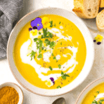 A bowl of paleo curried butternut squash soup garnished with flowers and fresh parsley.