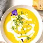 A bowl of curried butternut squash soup garnished with fresh parsley and fresh flowers.