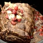 A cooked beef roast in a slow cooker, topped with onions and cranberries.