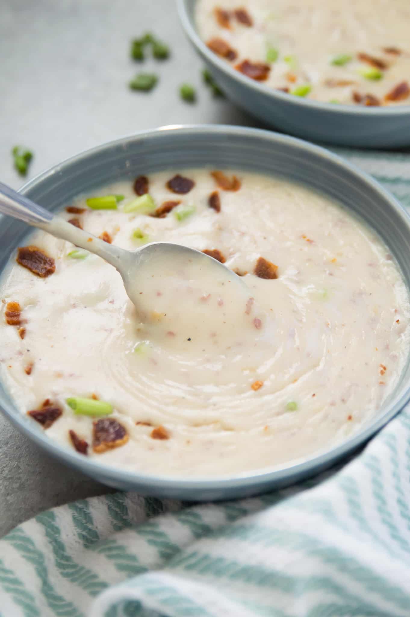 A bowl of creamy dairy free potato soup that is topped with chopped bacon, chives and has a spoon in it.