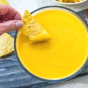 A bowl of vegan cheese sauce with a chip being dipped into it.