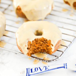 A carrot cake donut with icing on it and a bite out of it.