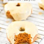 A carrot cake donut on a baking rack with a bite out of it.