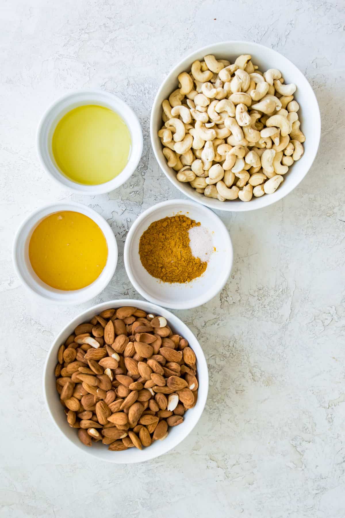 The ingredients needed to make homemade curry cashews and almonds in small bowls. 