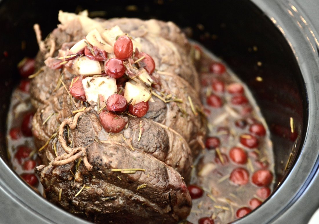 A beef roast in a slow cooker topped with cranberries and onions 