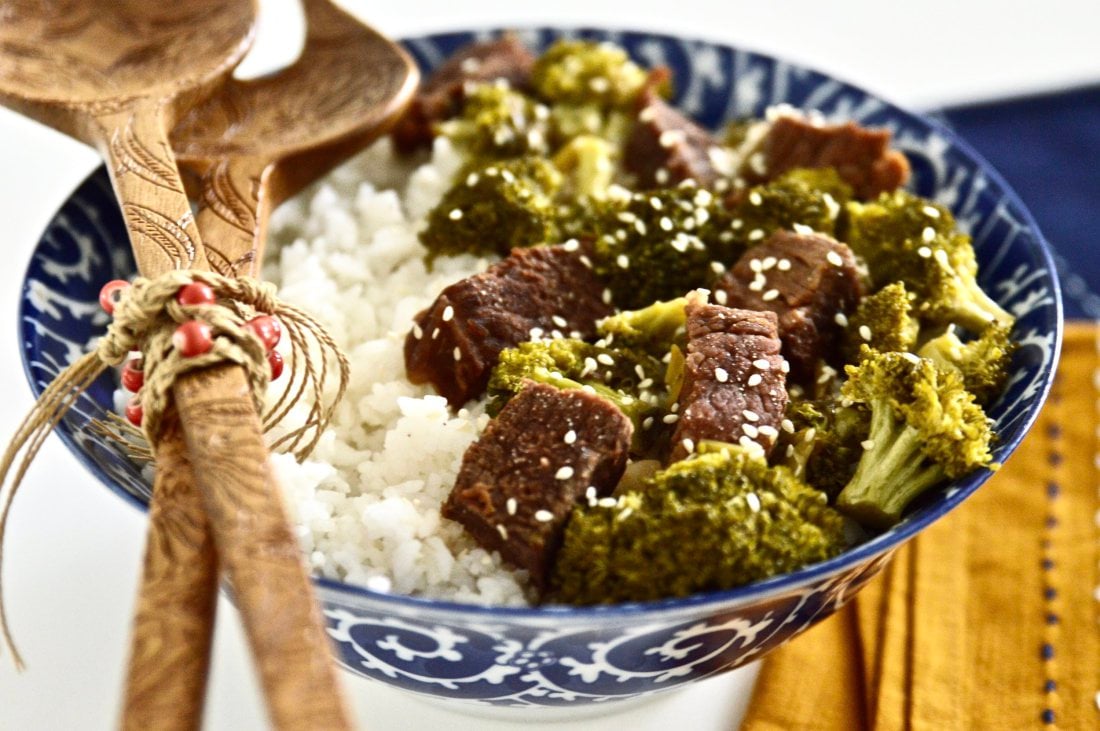 A large bowl of beef and broccoli served over white rice and topped with sesame seeds. 