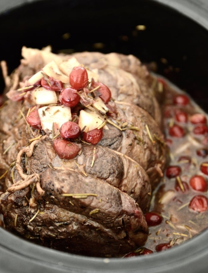 A cranberry beef roast in a slow cooker topped with onions and cooked cranberries. 