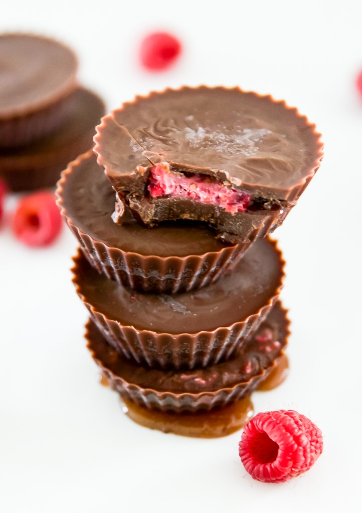 A stack of chocolate raspberry cups with raspberries surrounding them.
