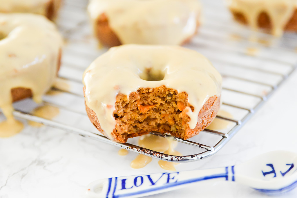 A carrot cake donut with icing on a baking rack with a bite out of it.