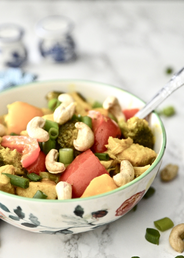A bowl of mango chicken curry topped with green onion and cashews