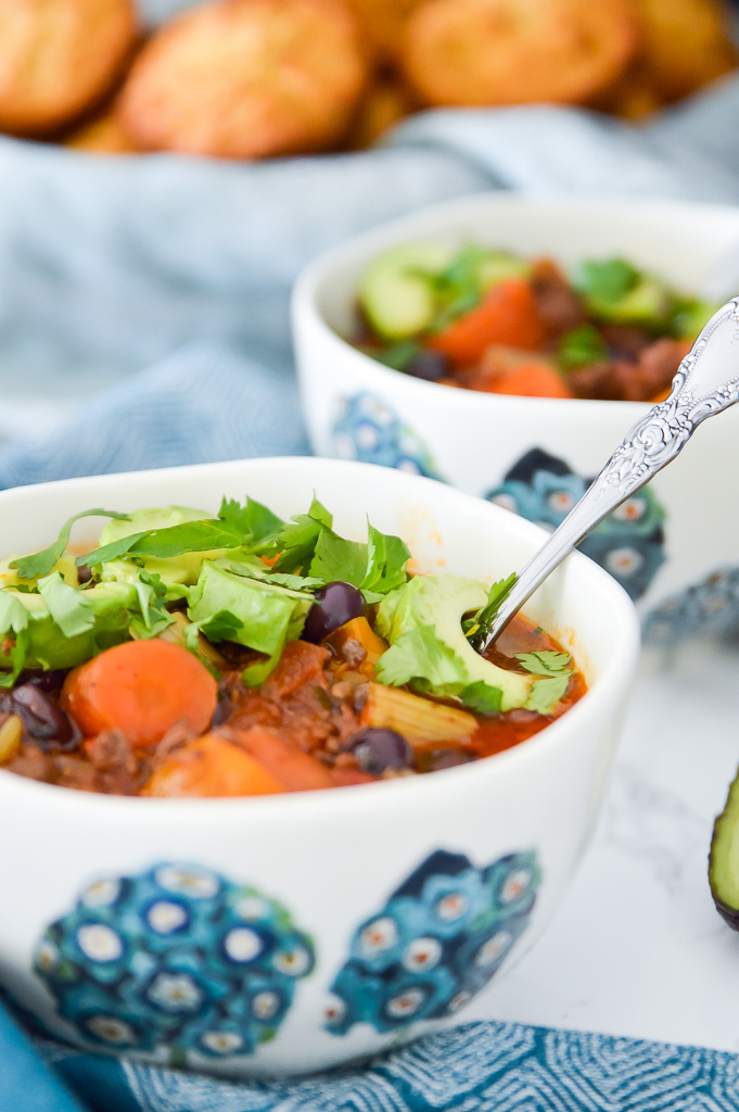 A bowl of chili with blueberries topped with avocado and fresh cilantro.