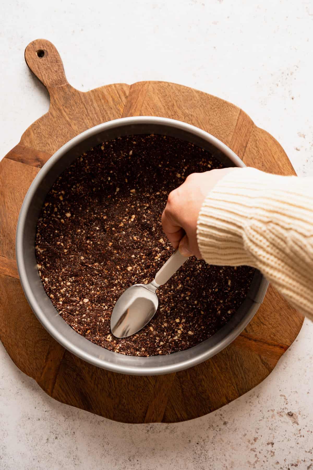A chocolate crust being pushed down into a round springform pan.