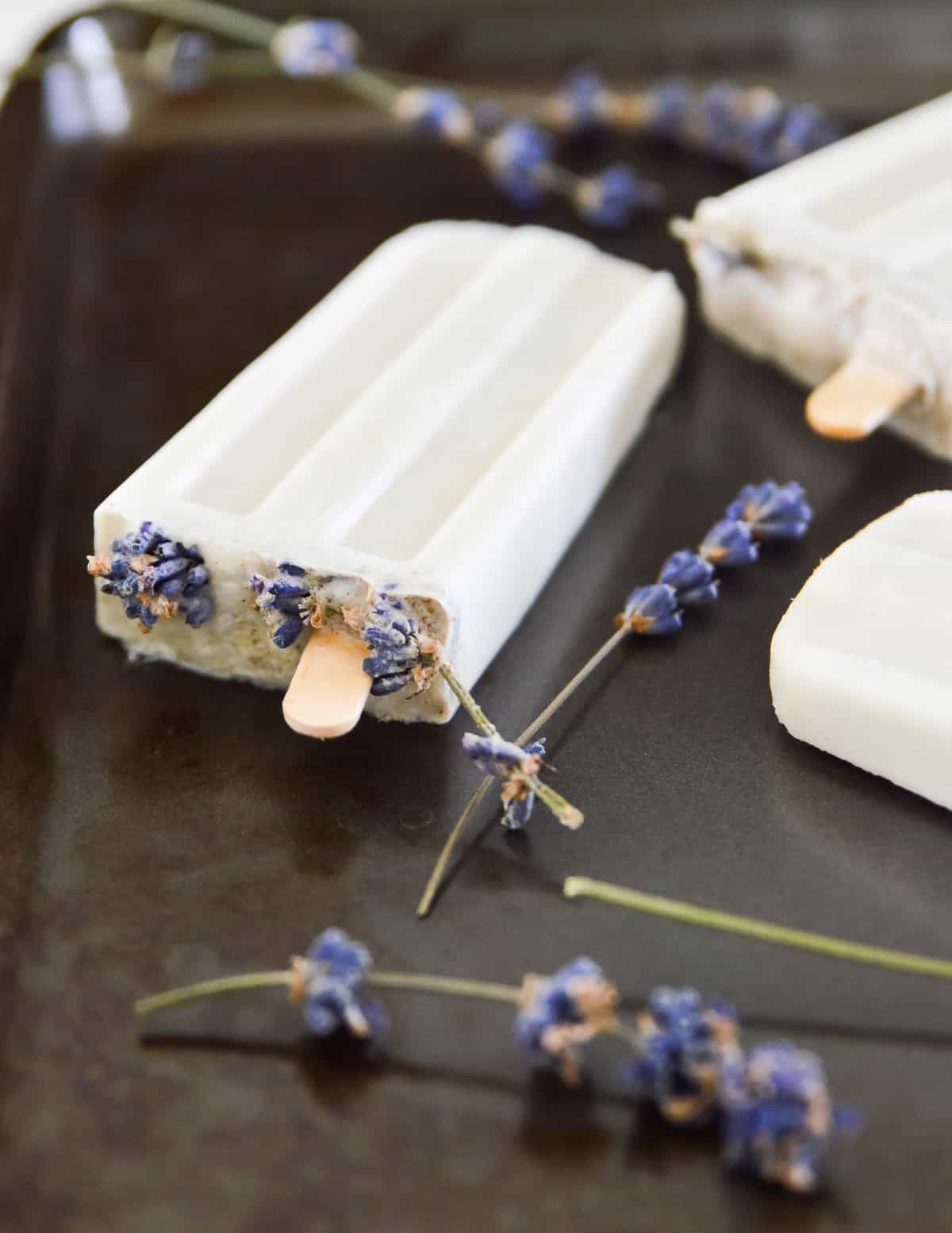 Lavender vanilla popsicles on a tray with dried lavender flowers around them. 