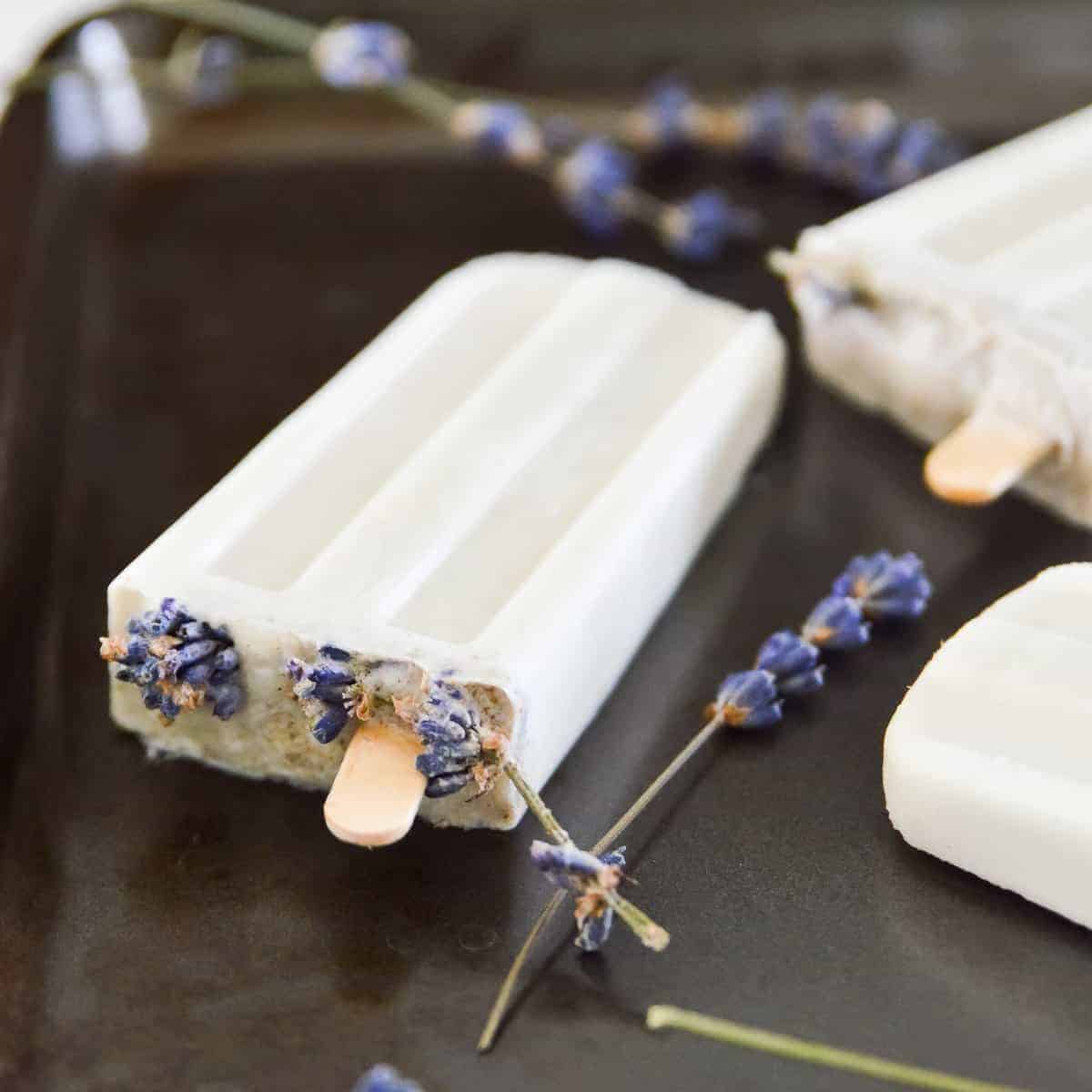 Lavender vanilla popsicles on a tray with lavender flowers around them.