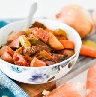 A bowl of paleo beef stew on a serving board with carrots and onions around it.