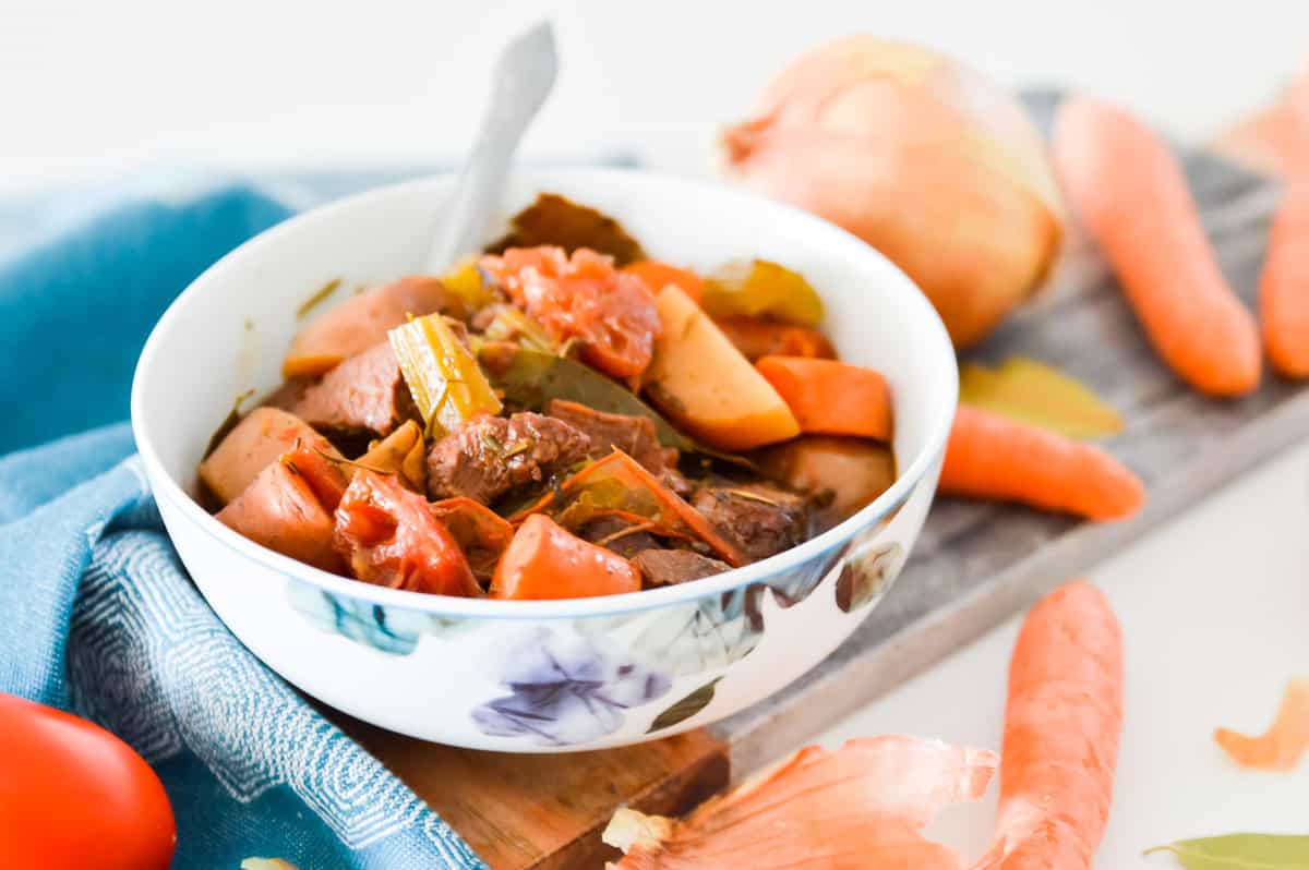 A bowl of beef stew with raw vegetables beside it.