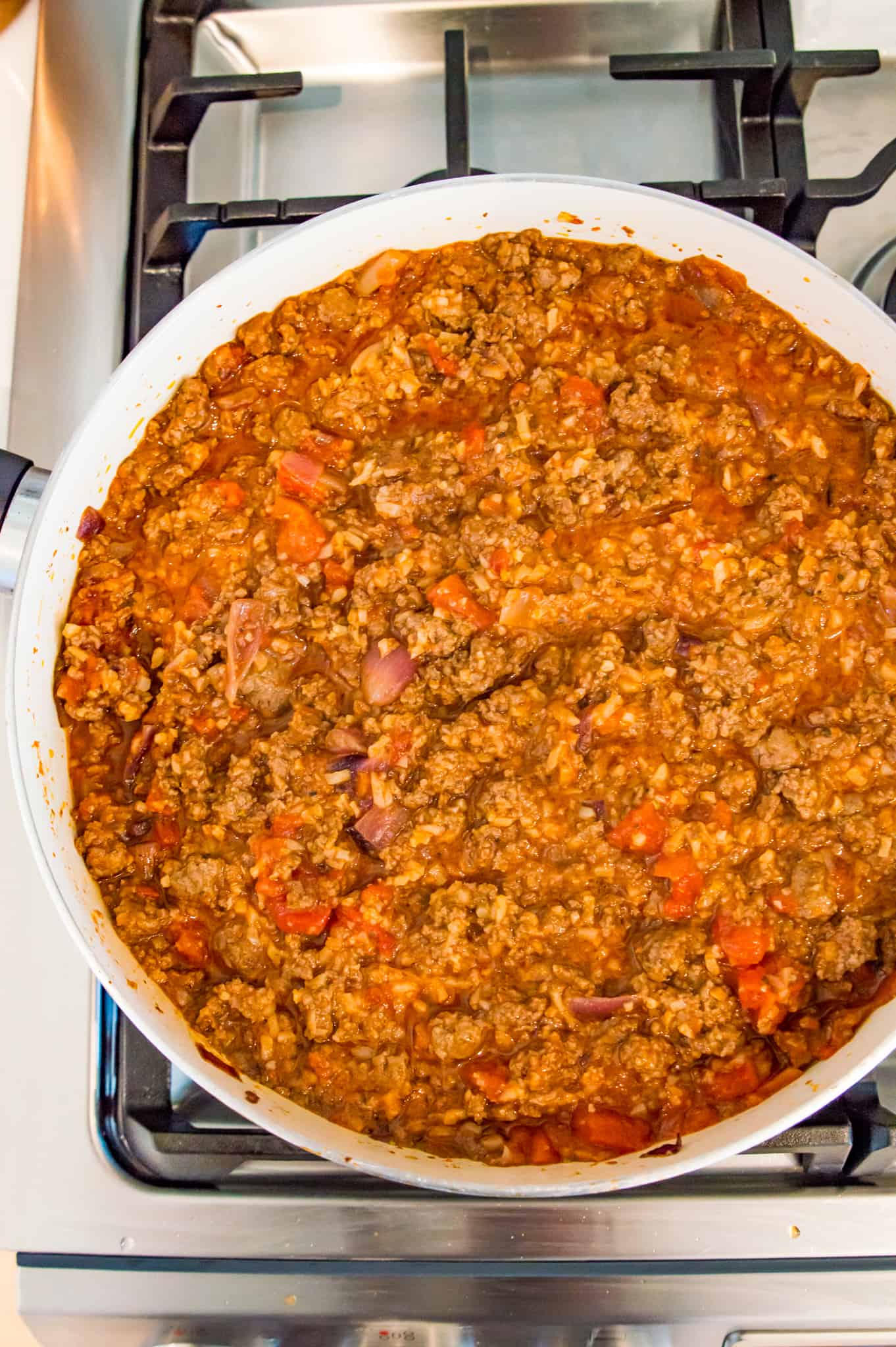 Ground beef, onions and tomatoes cooking in a frying pan on the stovetop.