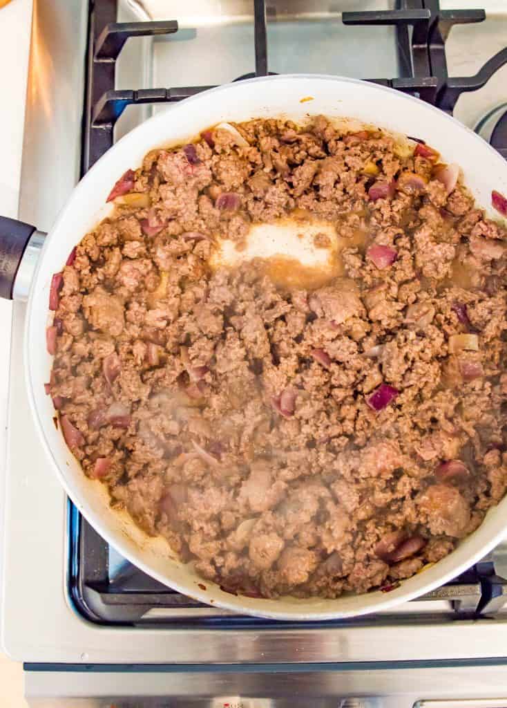 Ground beef and onions being cooked in a frying pan on the stovetop.