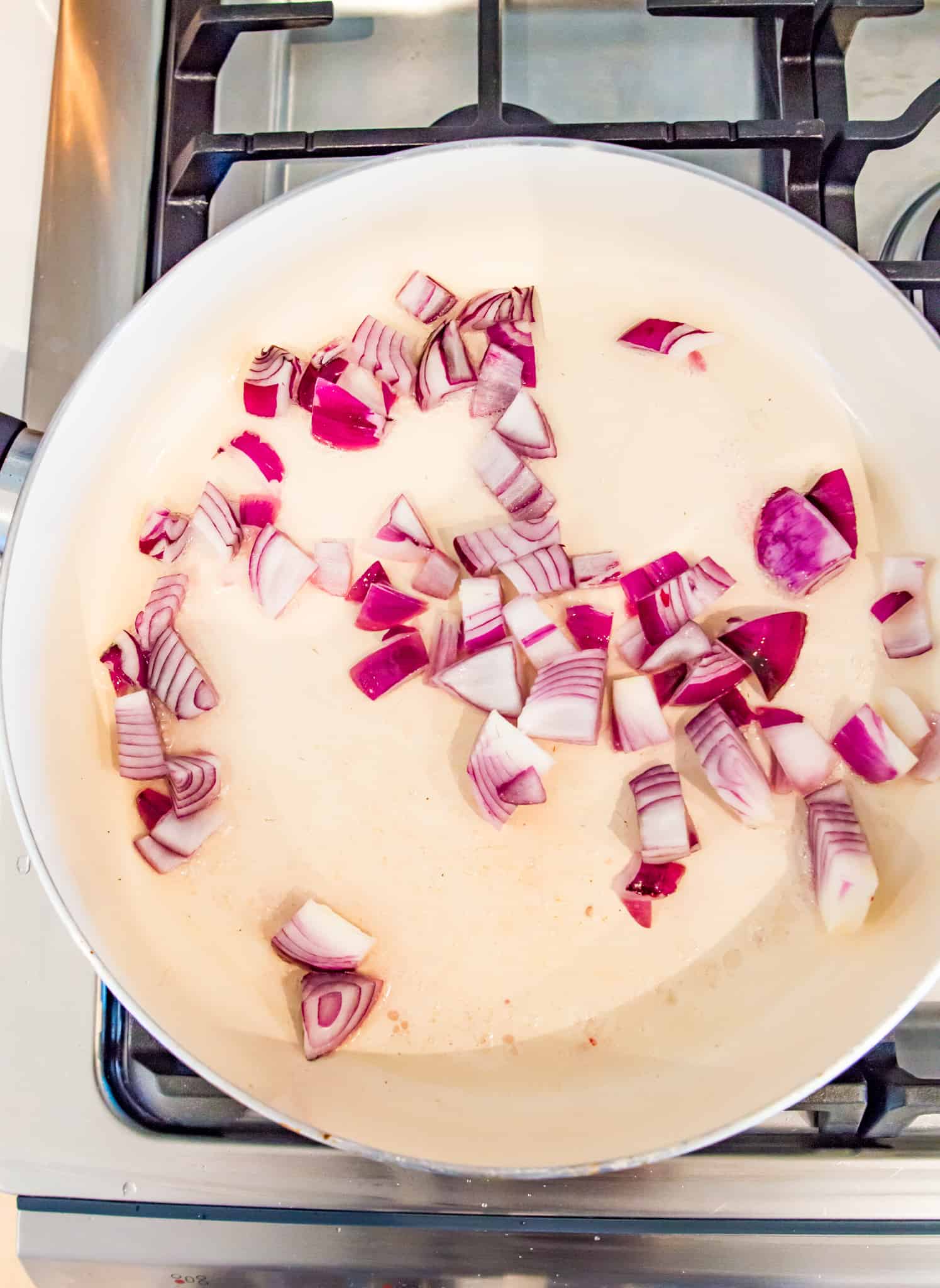 Chopped onions being cooked in a frying pan on the stovetop. 