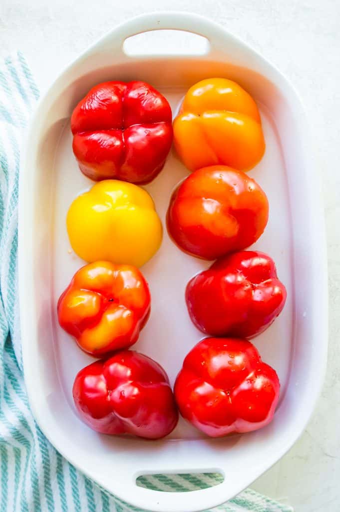 Bell peppers that have been cut in half in a casserole dish with some water.