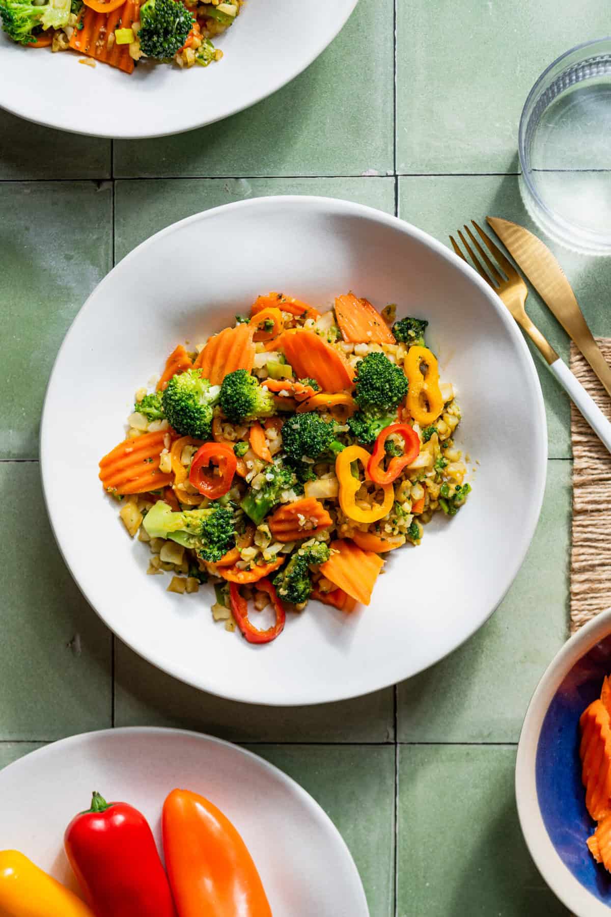 A plate with cauliflower fried rice in it topped with chopped bell peppers and broccoli florets.