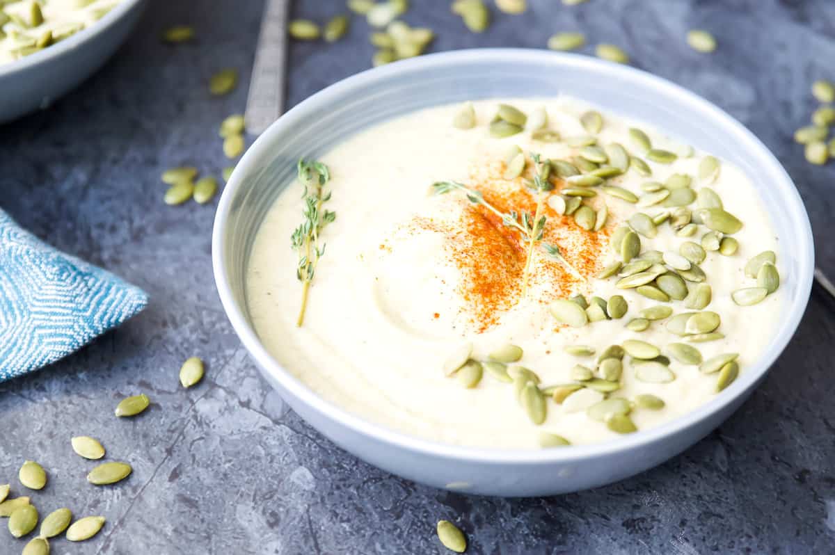 A bowl of cauliflower soup topped with pumpkin seeds and fresh thyme.