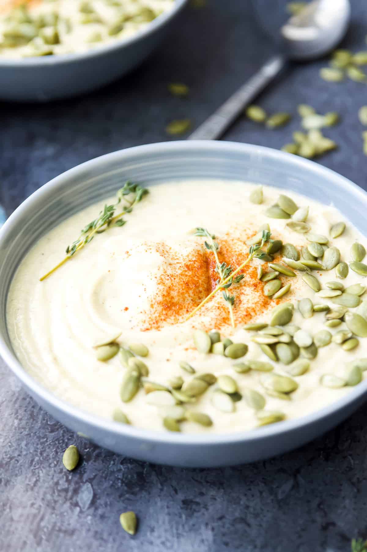 A large bowl of cauliflower soup with raw pumpkin seeds and fresh thyme on it.