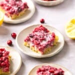 Cranberry lemon bars on plates with lemons and cranberries around them.