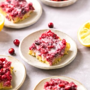 Gluten free cranberry lemon bars on plates with lemons and cranberries around them.