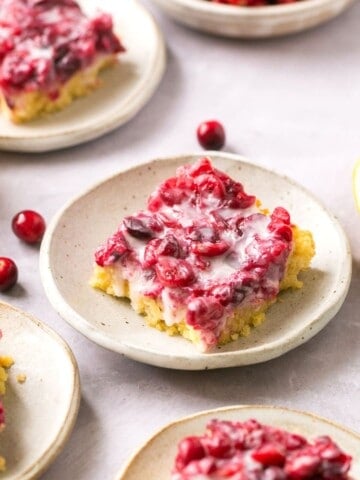 Gluten free cranberry lemon bars on plates with lemons and cranberries around them.