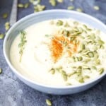 A bowl of vegan cauliflower soup topped with pumpkin seeds and fresh sage.