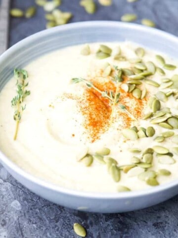 A bowl of vegan cauliflower soup topped with pumpkin seeds and fresh sage.