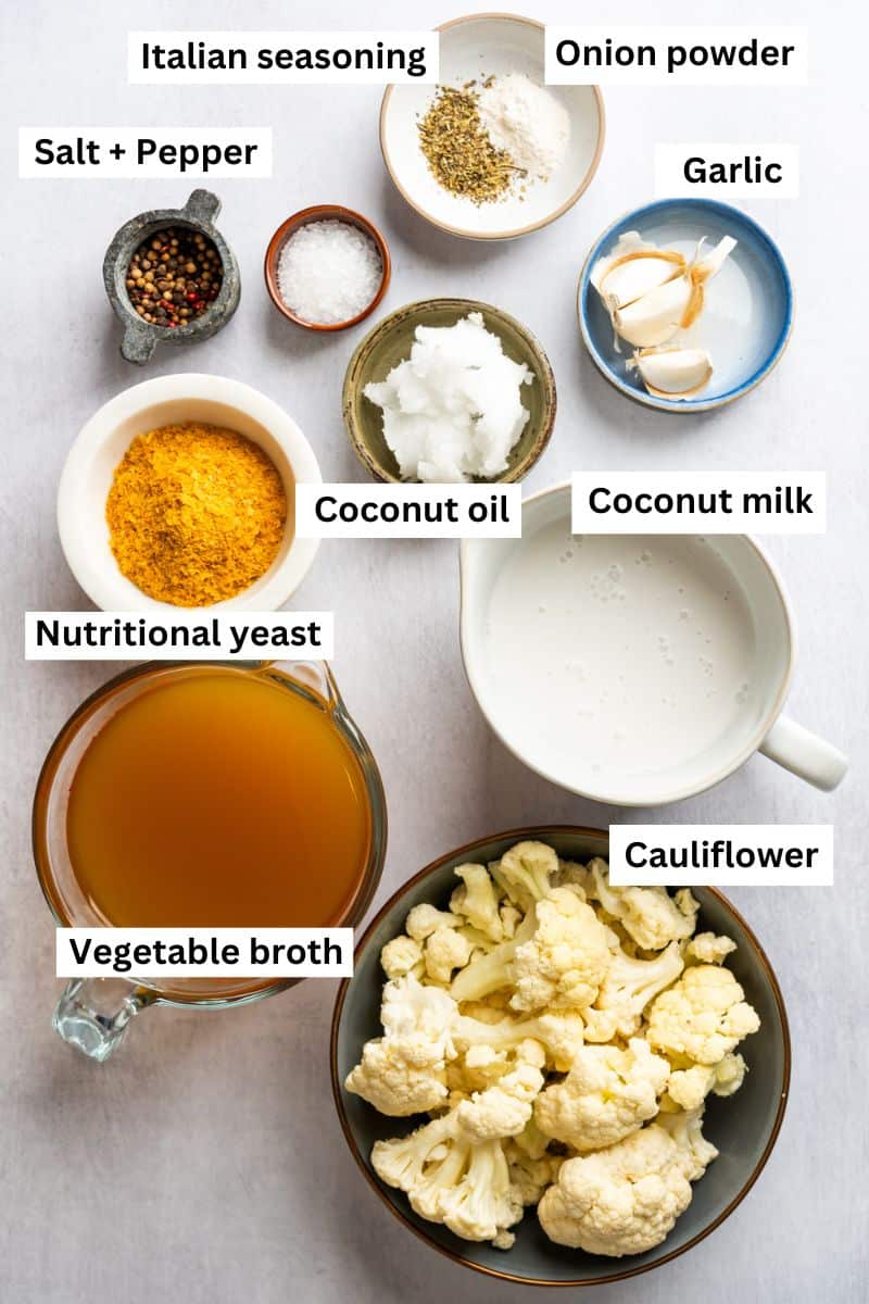 The ingredients needed to make a vegan cauliflower soup separated into bowls including cauliflower, broth, garlic, nutritional yeast and spices.