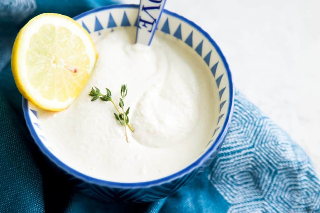 A bowl of vegan sour cream with sprigs of rosemary and a lemon slice on top