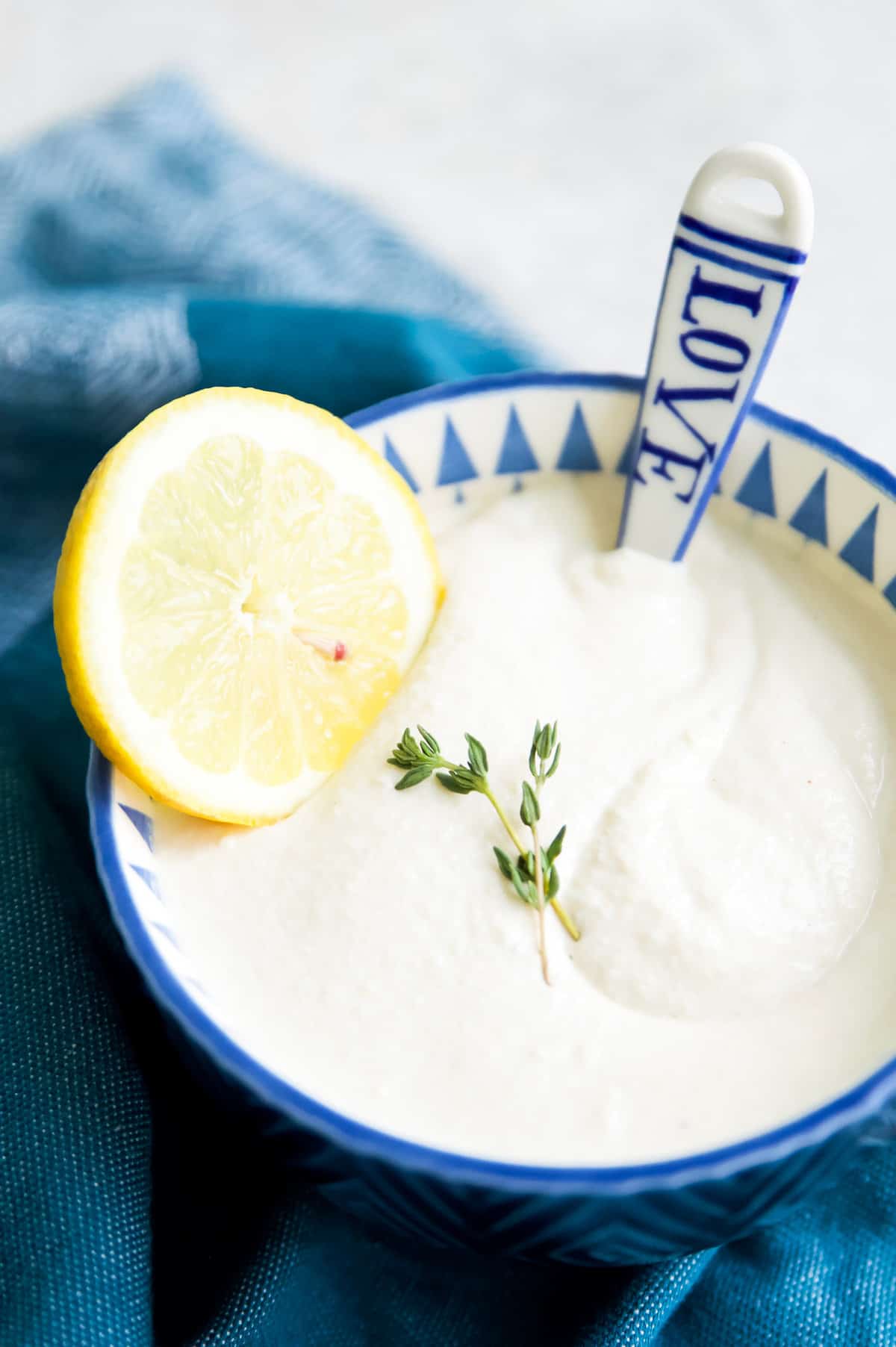 A bowl of dairy free sour cream with a lemon slice and a spoon.