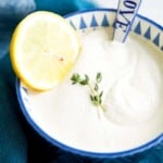 A bowl of dairy free sour cream with a spoon in it and a lemon slice on top.