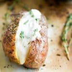 A baked potato with herbs topped with vegan sour cream