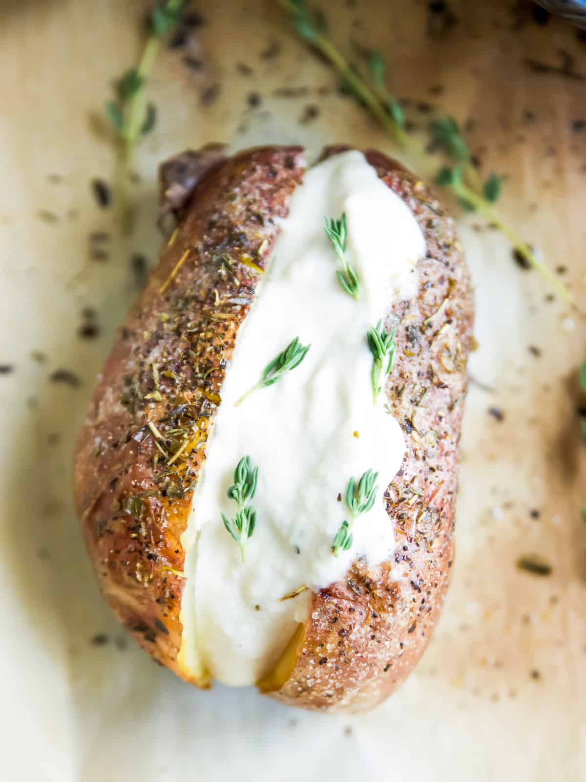 A baked potato topped with vegan sour cream and fresh rosemary.
