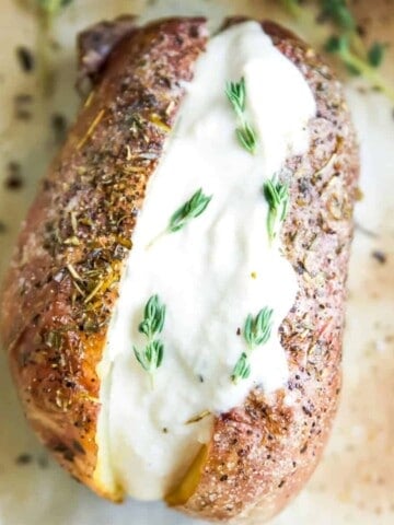 A baked potato with herbs topped with vegan sour cream and fresh rosemary.