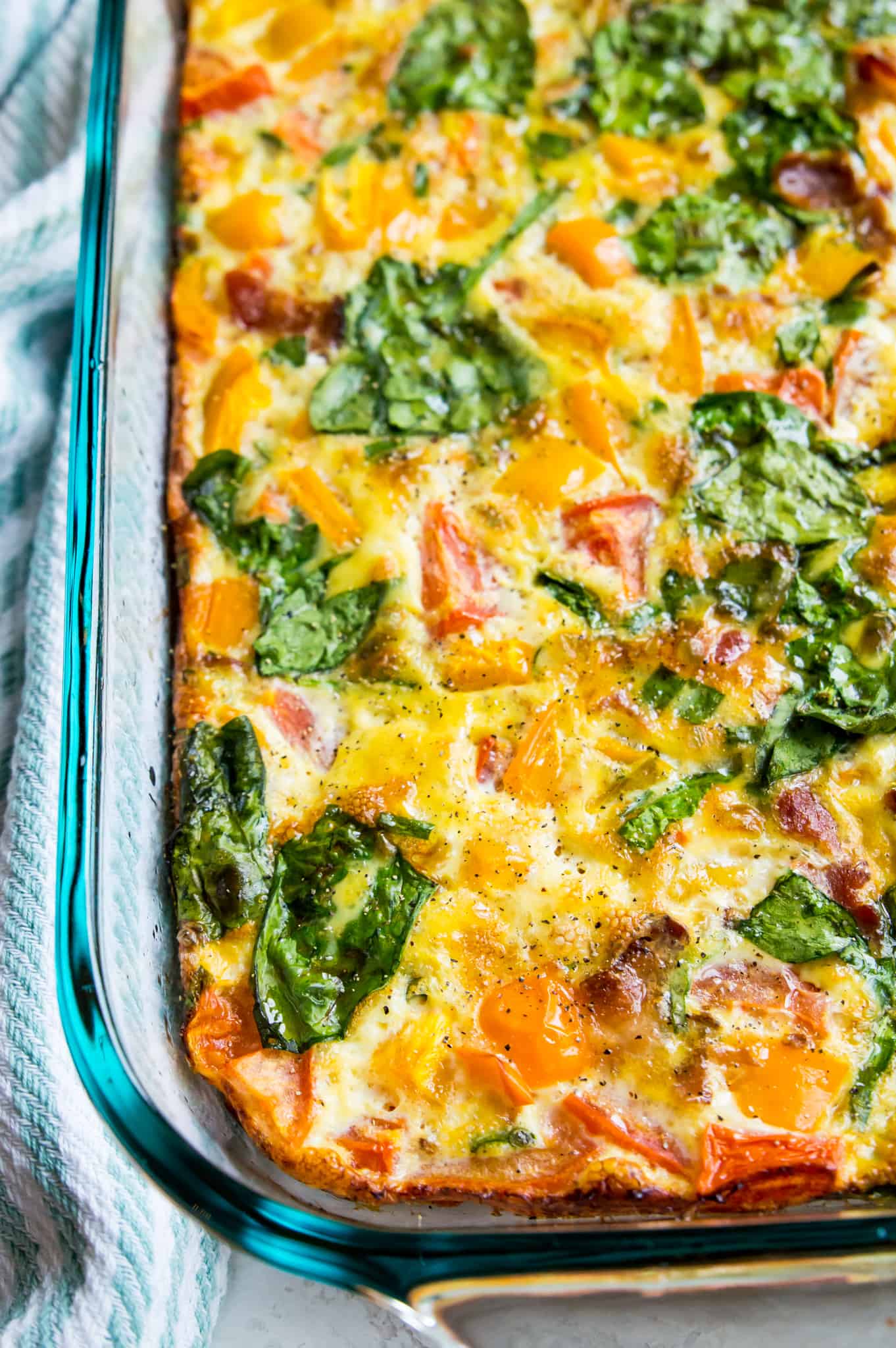 A pan filled with a cooked bacon and vegetable egg casserole with spinach, peppers and spices in it.